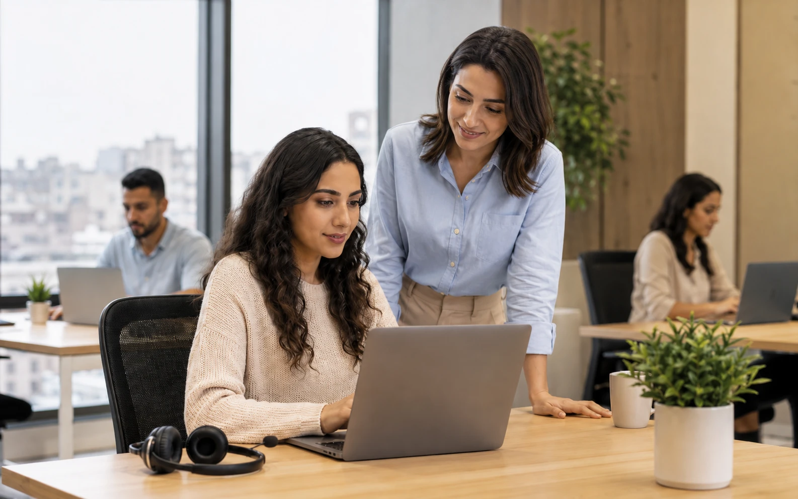 An Ant Assist team leader reviewing a virtual assistant's work on her laptop in the Cairo office, with two colleagues working at desks behind them.